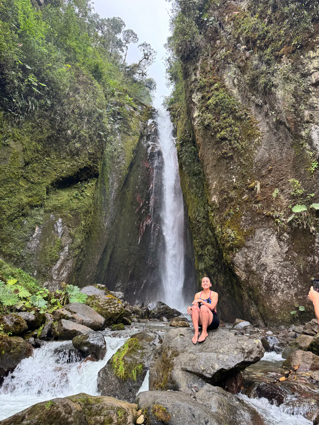 Mujer sonriente sentada frente a una cascada en la montaña